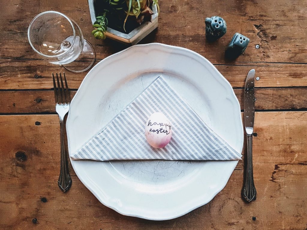 Easter egg on white plate with fork and knife on wooden table